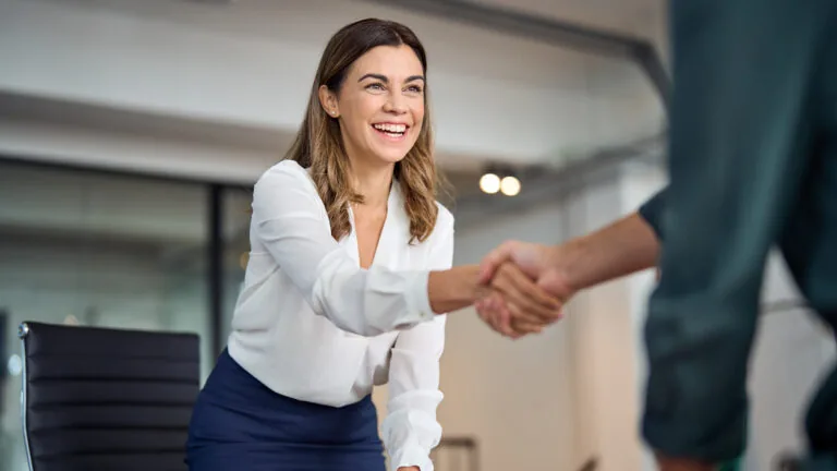 Happy mid aged business woman manager handshaking greeting client in office.